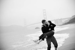 An engagement kiss on the beach by the Golden Gate Bridge in San Francisco, California.