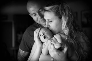 In Coloma, California, a newborn is held by her adoring parents in the window light.