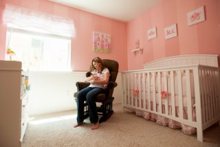 A new mother rocks her baby to sleep in a cute pink nursery in Sacramento, California.